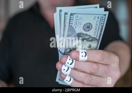 Un homme adulte tient sa main avec $100 billets à l'appareil photo. Les premières phalanges de ses doigts sont enveloppées dans un ruban blanc. Les visages souriants sont douloureux Banque D'Images