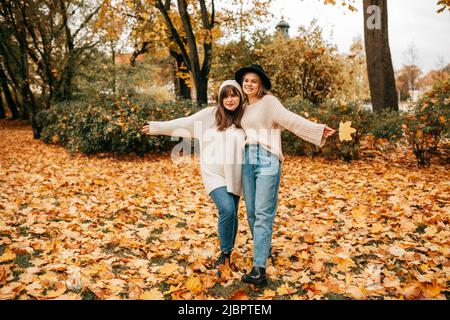 Deux jeunes amies ont du plaisir dans le parc en posant leurs bras autour l'un de l'autre et les bras débordés. Ils sont vêtus de jeans bleus et Banque D'Images