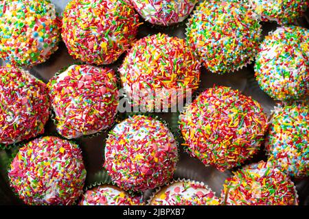 Cupcakes maison décorés de saupoudres de sucre vue de dessus. Groupe de muffins à la vanille faits maison décoration multicolore blanche émaillée. Fond de gâteau sucré. Banque D'Images