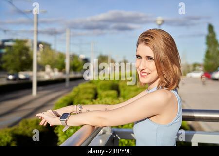 Femme regardant l'appareil photo et souriant en se tenant debout à l'extérieur dans la rue. Concept de style de vie urbain. Banque D'Images