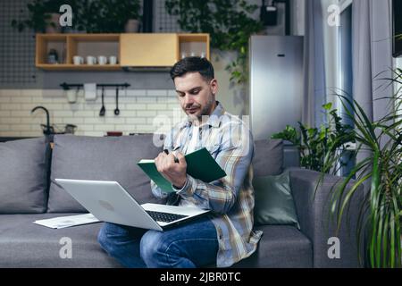 Un homme étudiant à la maison en ligne utilise un ordinateur portable, assis sur le canapé souriant Banque D'Images