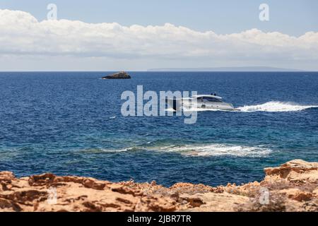Petit bateau à moteur argenté se déplace le long de la côte jaune rocheuse de l'île d'Ibiza. Mer calme la plus claire et ligne horizontale de nuages blancs solides à l'horizon Banque D'Images