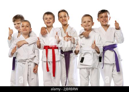 Groupe d'enfants heureux, jeunes combattants de karaté dans des doboks blancs debout ensemble isolés sur fond blanc. Concept de sport, arts martiaux Banque D'Images