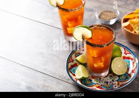 Cocktail de michelada maison avec bière, jus de lime, sauce chaude, plateau salé et jus de tomate sur table en bois Banque D'Images