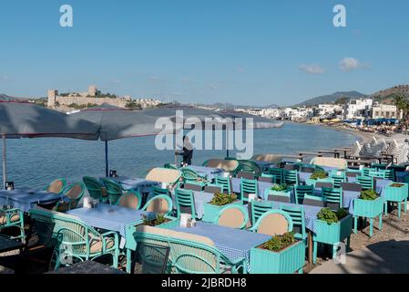 Bodrum, Mugla, Turquie. 21 avril 2022 Un serveur prépare des tables sur le café de la plage dans le port de Bodrum avec le château de Bodrum en arrière-plan, l'AEG Banque D'Images