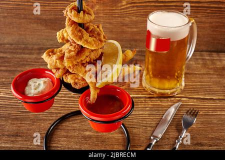 Rondelles de calmar en pâte avec des sauces au citron, rouges et blanches sur une table en bois Banque D'Images