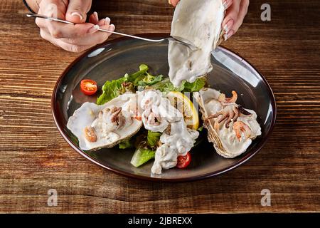 Fruits de mer. Cuisine de restaurant, nourriture saine et raffinée. Huîtres, crevettes, poulpe dans une sauce à la crème blanche dans la coquille d'huîtres. Banque D'Images