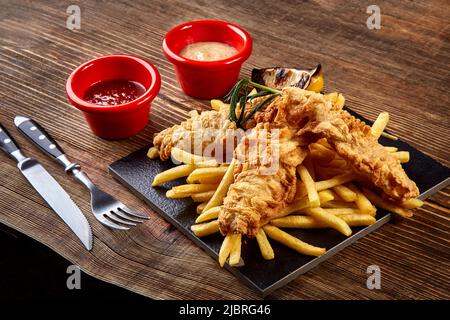 Assiette noire avec poisson et chips, mayonnaise et ketchup sur fond de bois Banque D'Images