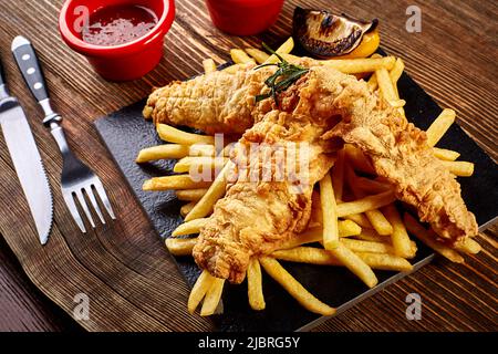 Assiette noire avec poisson et chips, mayonnaise et ketchup sur fond de bois Banque D'Images