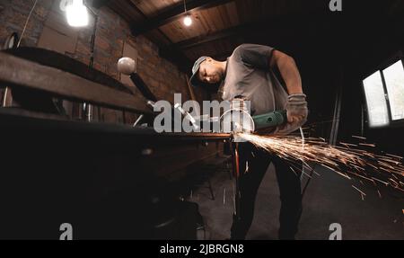 Un homme travaille avec une meuleuse d'angle dans son atelier à domicile. Fabriquer des produits métalliques avec vos propres mains Banque D'Images