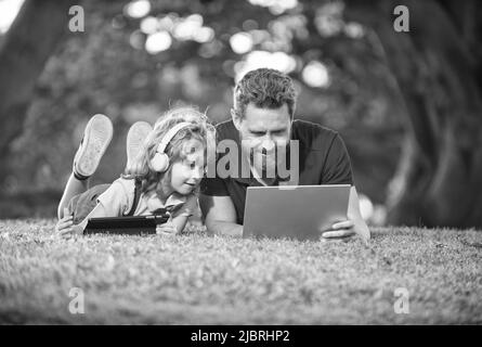 une famille heureuse de papa et de fils utilise un ordinateur portable et des écouteurs dans le parc, week-end familial. Banque D'Images