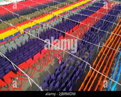 8 juin 2022, Narayanganj, Dhaka, Bangladesh : les travailleurs pendent des milliers de mètres de tissus de différentes couleurs pour sécher. Les fils de fer sont utilisés entre les cadres de bambou pour créer des lignes de lavage géantes pour la dernière partie du processus de mort que les tissus sont séchés au soleil. Fils lumineux de bleu, rose, orange, rouge, violet, des chiffons teints jaune, magenta et vert sont suspendus au-dessus du champ herbacé dans un réseau éblouissant de couleurs entrelacés. C'est la dernière partie du processus de mort après laquelle le tissu est fait chaque jour en t-shirts et gilets, qui sont ensuite vendus localement et internationalement. ( Banque D'Images