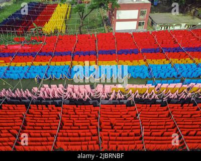 8 juin 2022, Narayanganj, Dhaka, Bangladesh : les travailleurs pendent des milliers de mètres de tissus de différentes couleurs pour sécher. Les fils de fer sont utilisés entre les cadres de bambou pour créer des lignes de lavage géantes pour la dernière partie du processus de mort que les tissus sont séchés au soleil. Fils lumineux de bleu, rose, orange, rouge, violet, des chiffons teints jaune, magenta et vert sont suspendus au-dessus du champ herbacé dans un réseau éblouissant de couleurs entrelacés. C'est la dernière partie du processus de mort après laquelle le tissu est fait chaque jour en t-shirts et gilets, qui sont ensuite vendus localement et internationalement. ( Banque D'Images