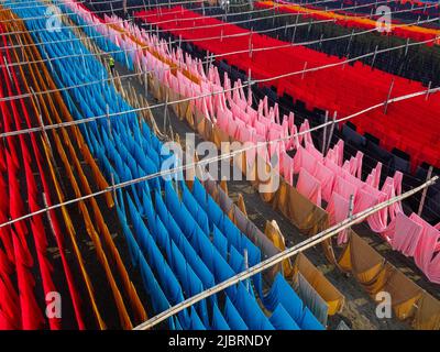 8 juin 2022, Narayanganj, Dhaka, Bangladesh : les travailleurs pendent des milliers de mètres de tissus de différentes couleurs pour sécher. Les fils de fer sont utilisés entre les cadres de bambou pour créer des lignes de lavage géantes pour la dernière partie du processus de mort que les tissus sont séchés au soleil. Fils lumineux de bleu, rose, orange, rouge, violet, des chiffons teints jaune, magenta et vert sont suspendus au-dessus du champ herbacé dans un réseau éblouissant de couleurs entrelacés. C'est la dernière partie du processus de mort après laquelle le tissu est fait chaque jour en t-shirts et gilets, qui sont ensuite vendus localement et internationalement. ( Banque D'Images