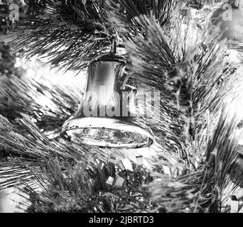 Décoration de Noël argentée brillante et métallique suspendue dans un sapin de Noël éclairé en noir et blanc Banque D'Images