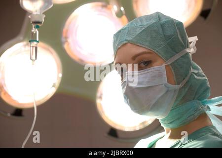 Une jeune femme est vue dans un théâtre d'opération de l'hôpital. Entièrement habillé comme une infirmière de théâtre avec un masque de visage et des vêtements de travail médicaux verts stériles. Banque D'Images