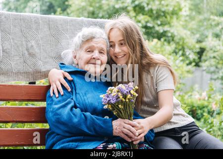 Jeune fille bénévole et aînée avec cadeau, bouquet de fleurs et panier d'épicerie Banque D'Images