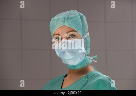 Une jeune femme est vue dans un théâtre d'opération de l'hôpital. Entièrement habillé comme une infirmière de théâtre avec un masque de visage et des vêtements de travail médicaux verts stériles. Banque D'Images