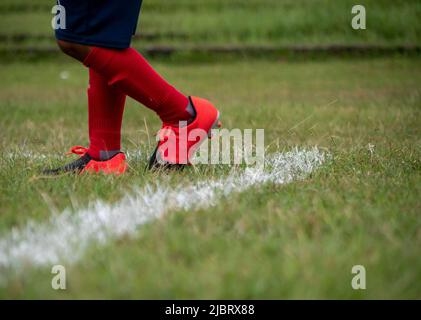 Joueur de football portant des chaussures de football marchant sur l'herbe avec une attention sélective. Banque D'Images