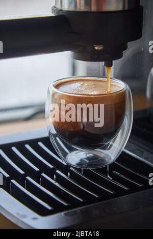 Faire du café frais sortant d'une machine à café espresso. Faire de l'expresso dans une tasse à café en verre transparent. Banque D'Images