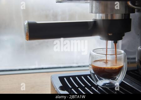 Faire du café frais sortant d'une machine à café espresso. Faire de l'expresso dans une tasse à café en verre transparent. Banque D'Images