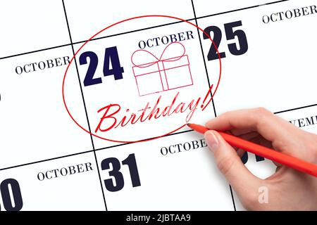 24th jour d'octobre. La main tourne la date sur le calendrier 24 octobre, dessine une boîte cadeau et écrit le texte anniversaire. Vacances. Automne mois, jour o Banque D'Images