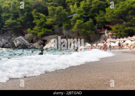 Plage de sable avec des vagues et des personnes nageant et appréciant les vibes d'été. Les gens et les antécédents sont hors foyer Banque D'Images