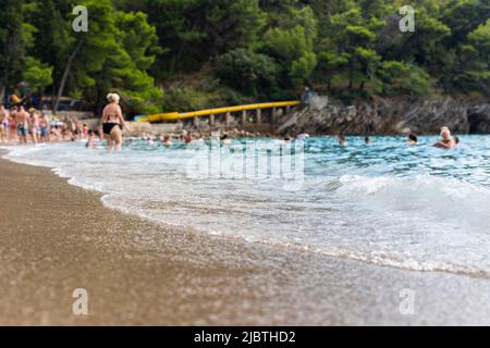 Plage de sable avec des vagues et des personnes nageant et appréciant les vibes d'été. Les gens et les antécédents sont hors foyer Banque D'Images