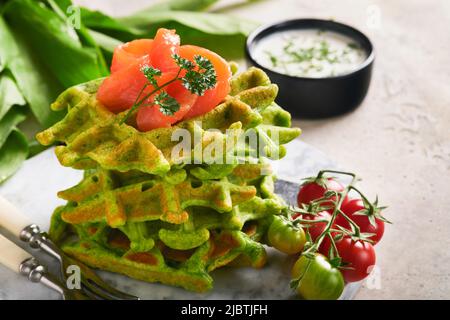 Gaufres belges vertes. Épinards ou ail sauvage ou gaufres au pesto avec saumon rouge et sauce à la crème sur fond de table en béton gris. Délicieux petit déjeuner, Banque D'Images