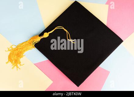 Casquette de remise de diplômes noire ou chapeau avec pampille jaune sur fond de couleur pastel éducation mortaboard Banque D'Images