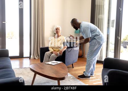 Médecin afro-américain examinant la pression artérielle d'une femme âgée de race blanche avec jauge à la maison Banque D'Images