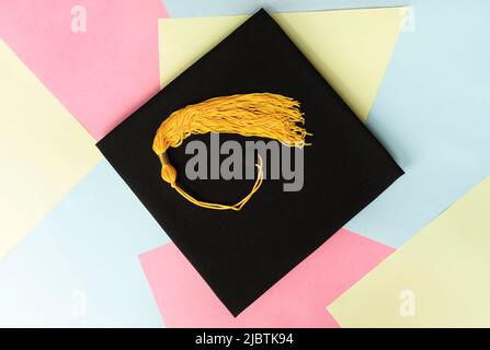 Casquette de remise de diplômes noire ou chapeau avec pampille jaune sur fond de couleur pastel éducation mortaboard Banque D'Images