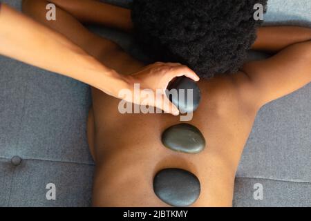 Femme afro-américaine recevant un massage aux pierres chaudes à la maison Banque D'Images