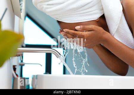Gros plan sur une femme afro-américaine lavant son visage dans le lavabo de la maison Banque D'Images