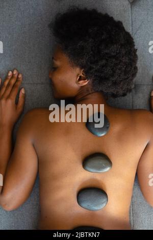 Femme afro-américaine avec les yeux fermés recevant un massage aux pierres chaudes à la maison Banque D'Images