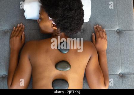 Femme afro-américaine avec les yeux fermés recevant un massage aux pierres chaudes à la maison Banque D'Images