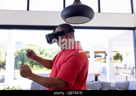 Vue latérale de l'homme âgé caucasien gestant tout en utilisant le simulateur de réalité virtuelle dans la maison de soins infirmiers Banque D'Images