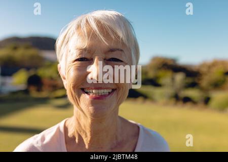 Portrait en gros plan d'une femme asiatique âgée gaie avec des cheveux courts contre le ciel bleu clair dans la cour Banque D'Images