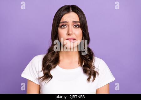 Photo de triste brunette jeune femme morsure lèvre porter t-shirt blanc isolé sur fond violet Banque D'Images
