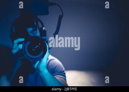 Gros plan d'un homme enregistrant des vidéos regardant à travers l'objectif. Appareil photo avec magnétoscope. Réduire la luminosité photo. Vue avant. Thème vidéographique. Banque D'Images