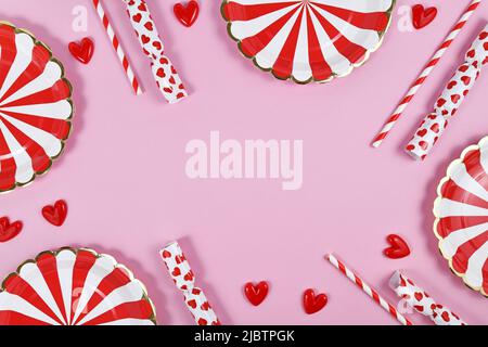 Bordure de fête avec assiettes en papier rouges, ornements en coeur, bonbons et pailles à boire sur fond rose avec espace de copie Banque D'Images