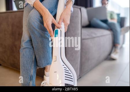 Les mains des femmes touchent l'aspirateur près du canapé Banque D'Images