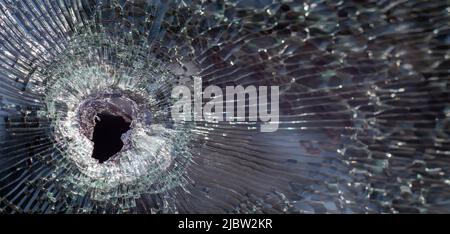 Trou de balle dans le verre avec des fissures, gros plan de trou de balle réel. La balle a fait un trou fissuré dans le pare-brise d'une voiture ou une vitre brisée comme Banque D'Images