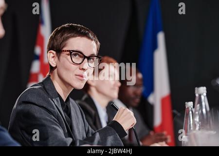 Portrait d'une jeune femme enceinte dans des lunettes regardant la caméra tout en parlant dans le microphone lors d'une conférence Banque D'Images