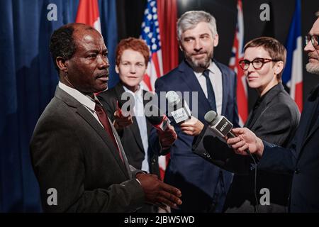 Homme politique africain mature donnant un entretien à des journalistes avec des microphones pendant une conférence de presse Banque D'Images