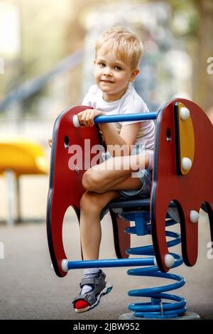 Portrait d'un garçon mignon sur un terrain de jeu sur un motif éléphant rouge balançant balançoire. Banque D'Images