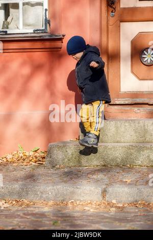 Un joli garçon dans une veste d'automne avec un chapeau bleu va pour une promenade dans la vieille ville. L'enfant escalade les escaliers. Banque D'Images