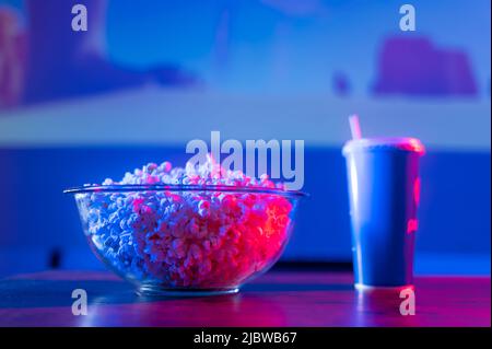 Gros plan. Pop-corn dans un bol en verre et une boisson gazeuse dans un verre avec une paille. Éclairage au néon. Repos, détente, regarder vos films préférés et T Banque D'Images