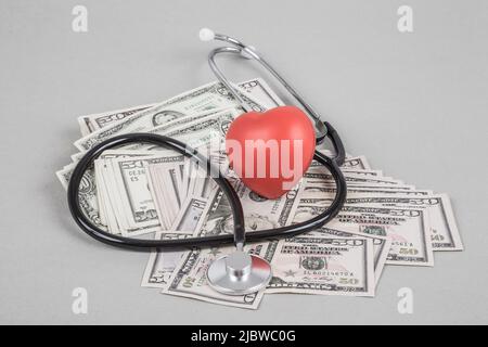 Un stéthoscope et un cœur rouge sur des dollars américains sur fond gris Banque D'Images