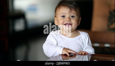 Adorable bébé se cachant sous la table. Bébé garçon souriant à l'appareil photo portrait jouant peekaboo Banque D'Images